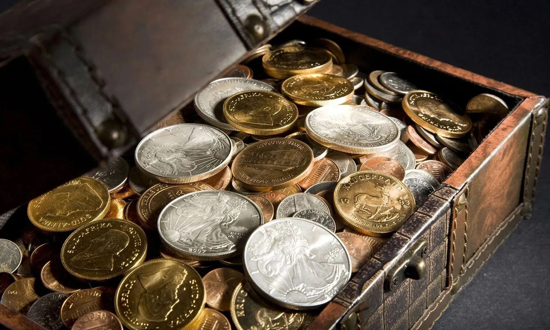 Open treasure chest filled with gold and silver coins on a dark surface