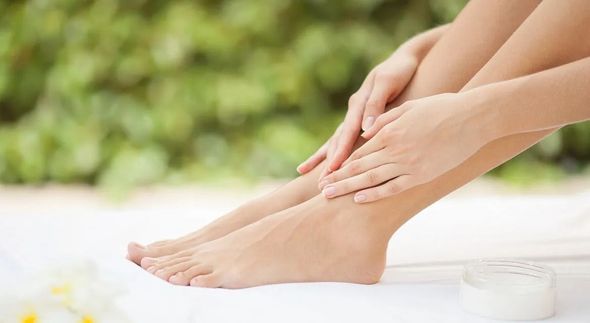Person applying lotion to legs, outdoors. White skin, greenery in background.