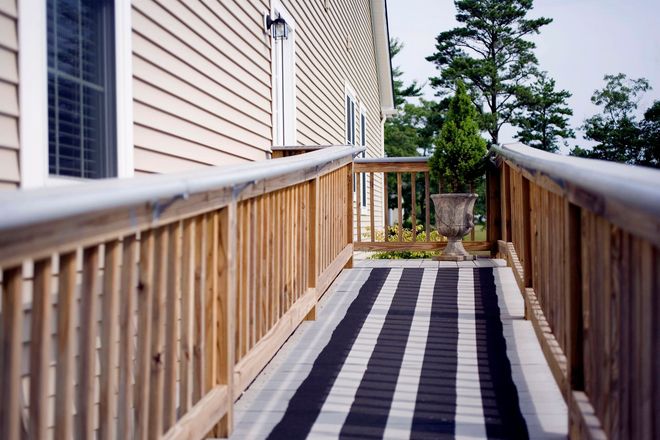 Wooden ramp beside a beige house, with a black-and-white striped runner and railing, leading to a garden.
