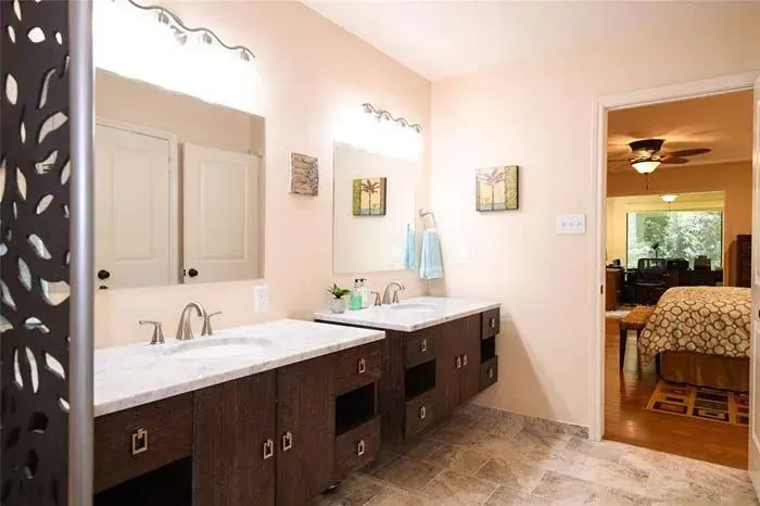 Spacious bathroom with double vanity, large mirror, and doorway to a bedroom beyond