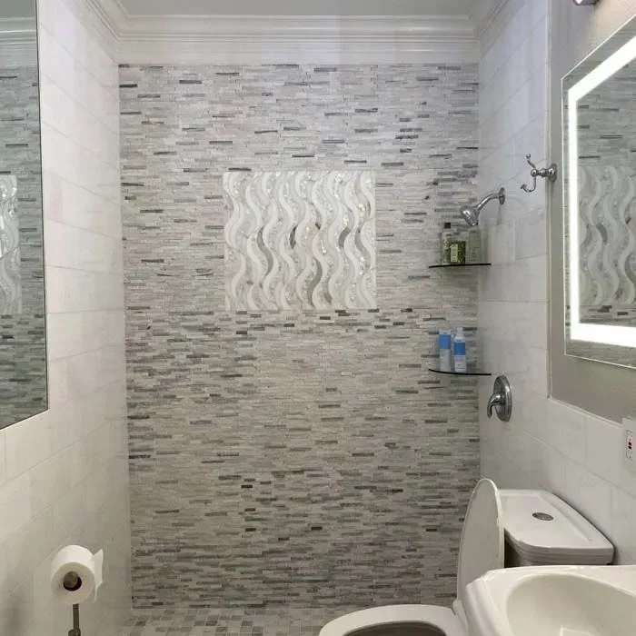 Modern tiled bathroom with a walk-in shower, toilet, and wall mirror.