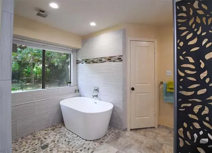 Modern bathroom with freestanding tub, large window, tiled walls, and patterned floor.