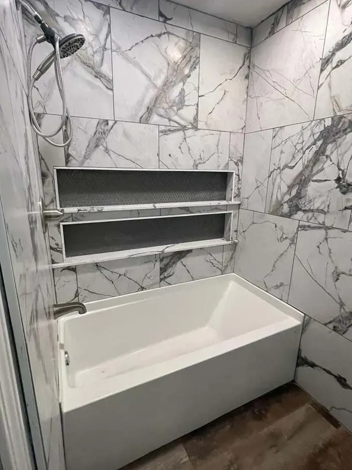 Modern bathroom with marble-pattern tile, built-in shelves, showerhead, and a white soaking tub.