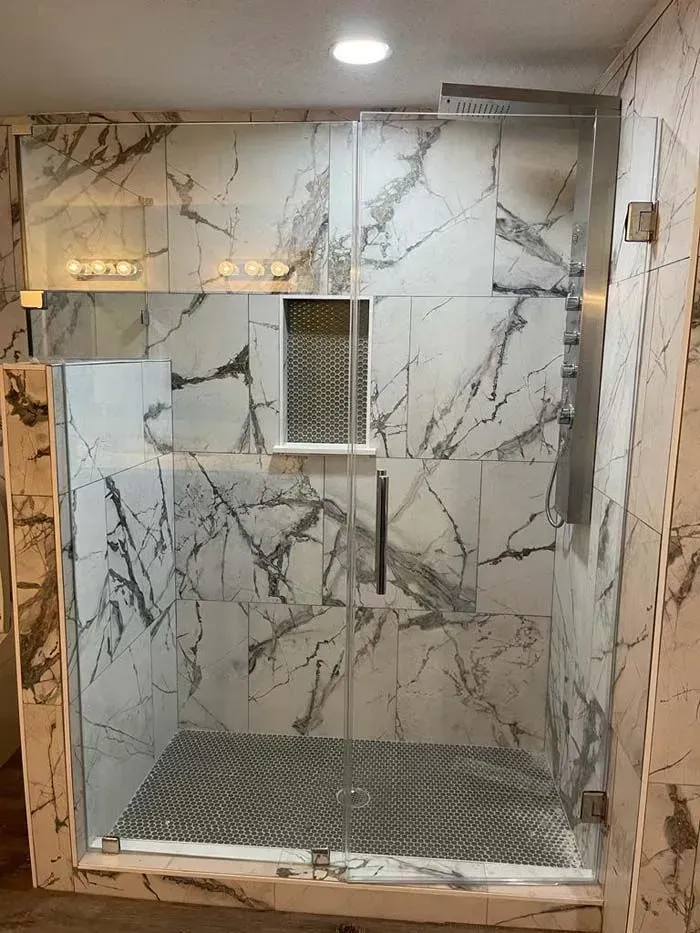 Marble-tiled shower stall with bench, overhead light, and metal drain grate