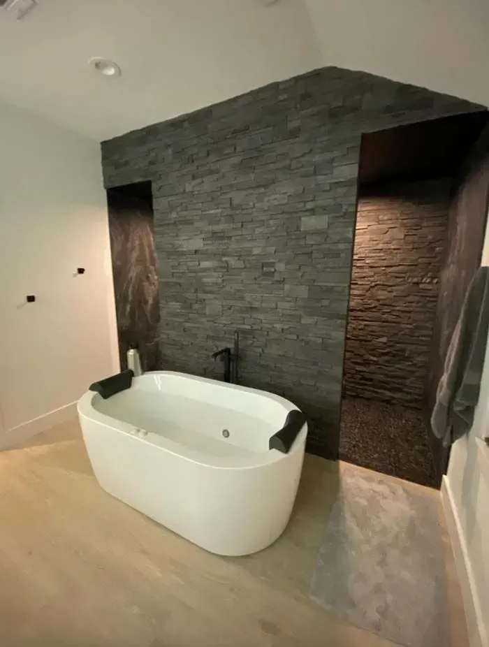 Modern bathroom with a freestanding white tub, dark stone accent wall, and built-in shower niches.