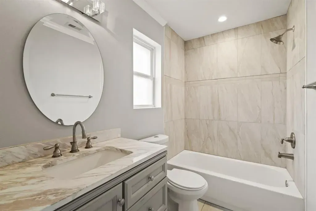 Bright modern bathroom with gray vanity, round mirror, tub, and beige tile shower walls