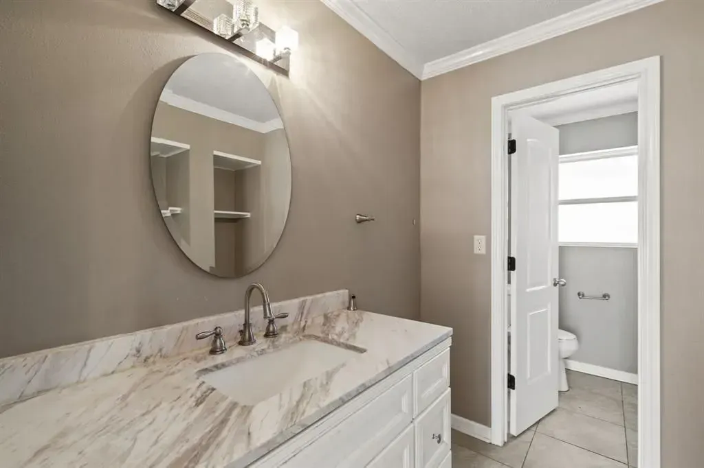 Modern bathroom vanity with round mirror and marble countertop, view toward a small adjacent room through an open door