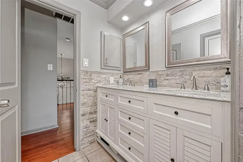 Bright modern bathroom with double vanity, large mirrors, and stone tile accents.