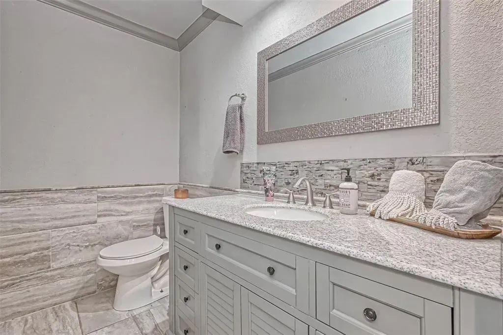 Elegant bathroom with gray vanity, granite countertop, large mirror, and tiled shower wall