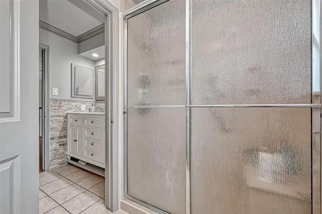 Bathroom with frosted glass shower door, white vanity, and tiled floor