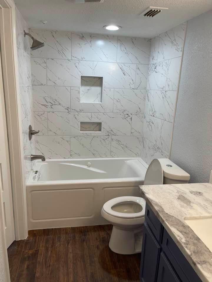 Accessible bathroom with white tub, tiled shower walls, toilet, and dark vanity floor.