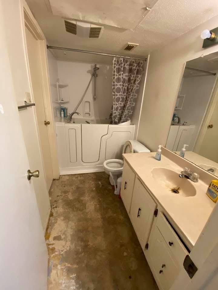 Narrow bathroom with tub and shower curtain, toilet, and long vanity sink under a large mirror.