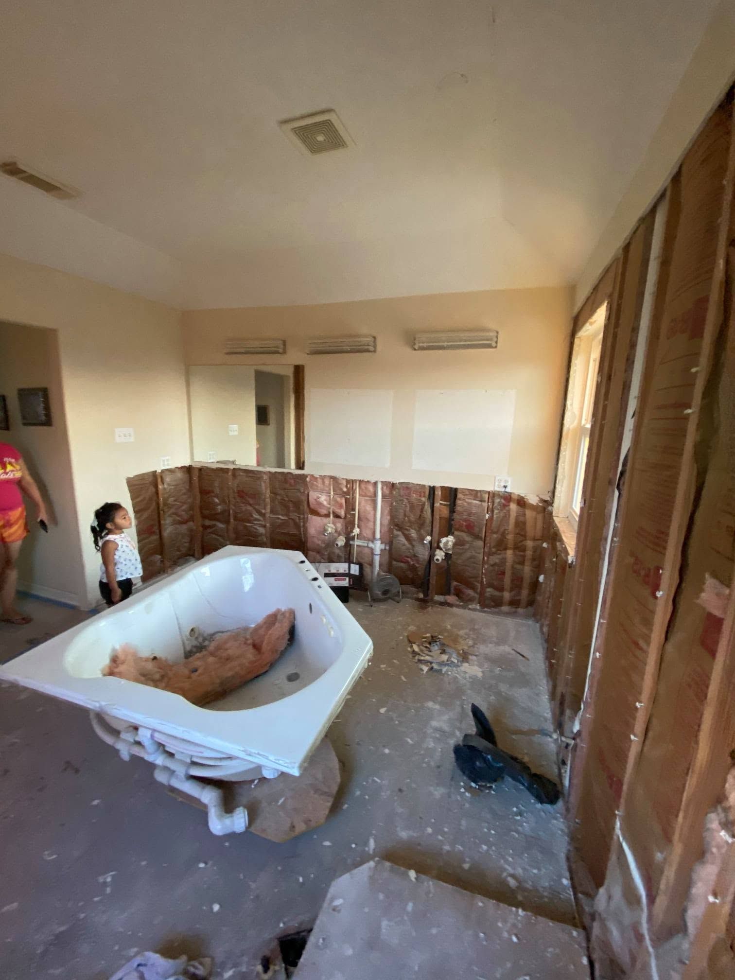 Bathroom under renovation with a bathtub, exposed wall studs, and construction debris on the floor.