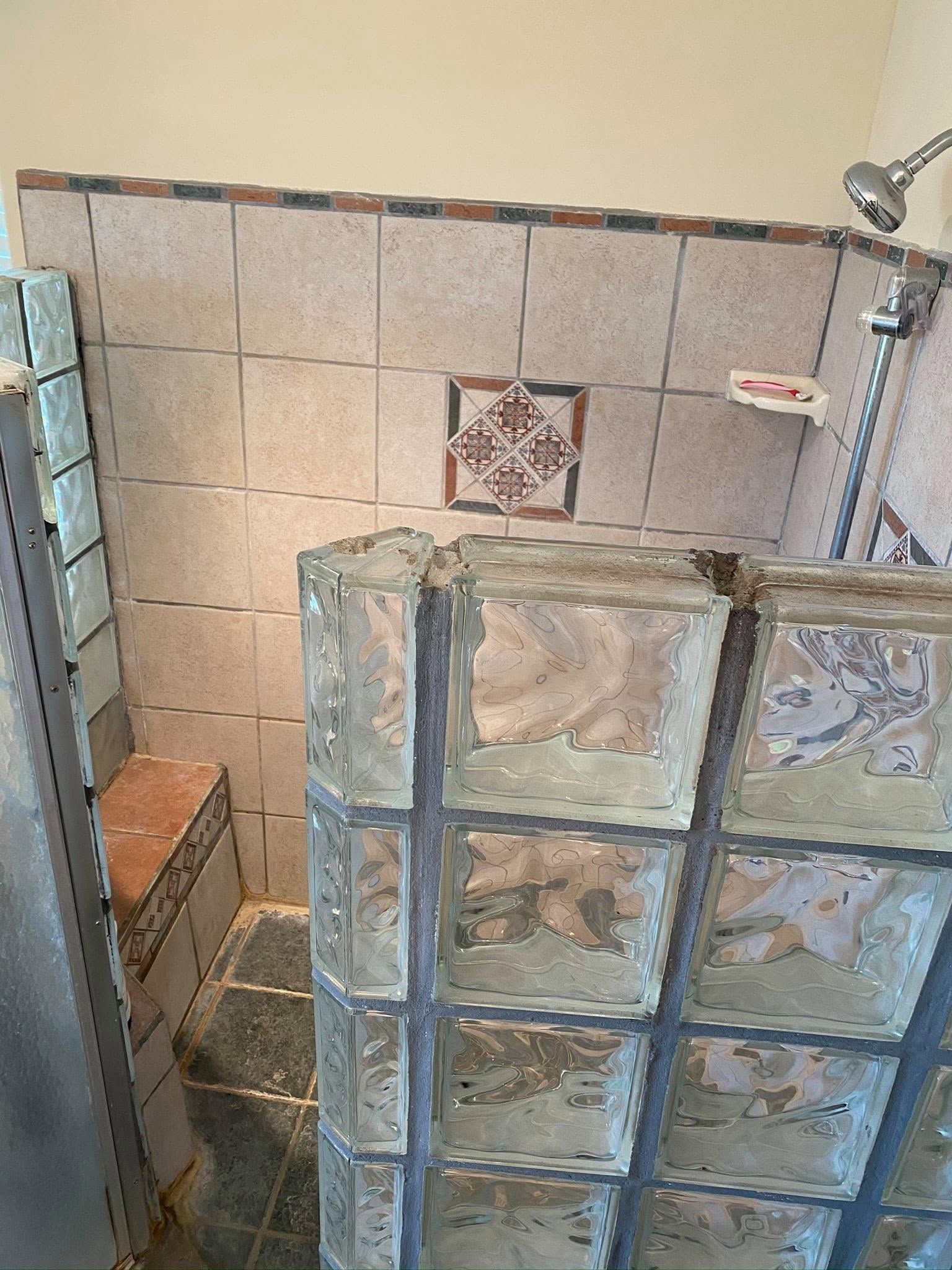 Tiled shower stall with blue-green glass-block wall and beige tile backdrop.