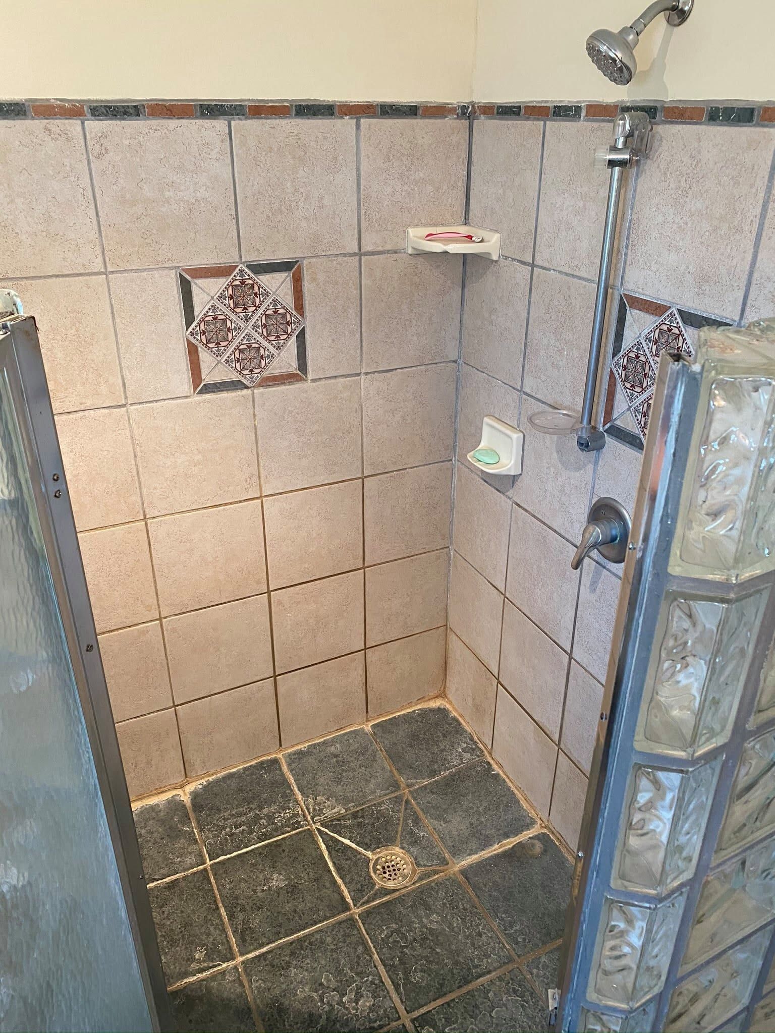 Tiled shower with wall-mounted showerhead, grab bar, and built-in shelf in a small bathroom.