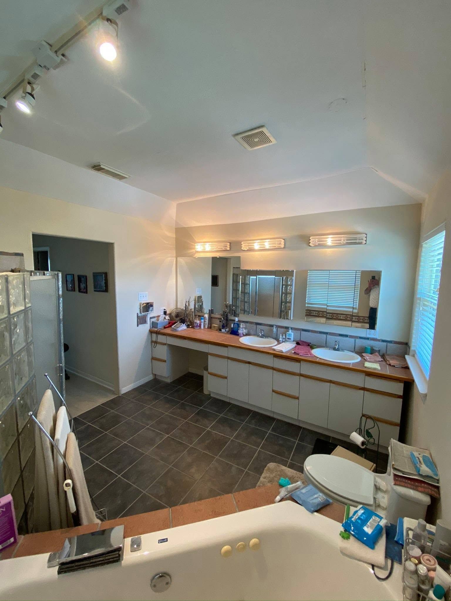 Spacious bathroom with a long vanity, large mirror, bright lights, tiled floor, and walk-in shower.