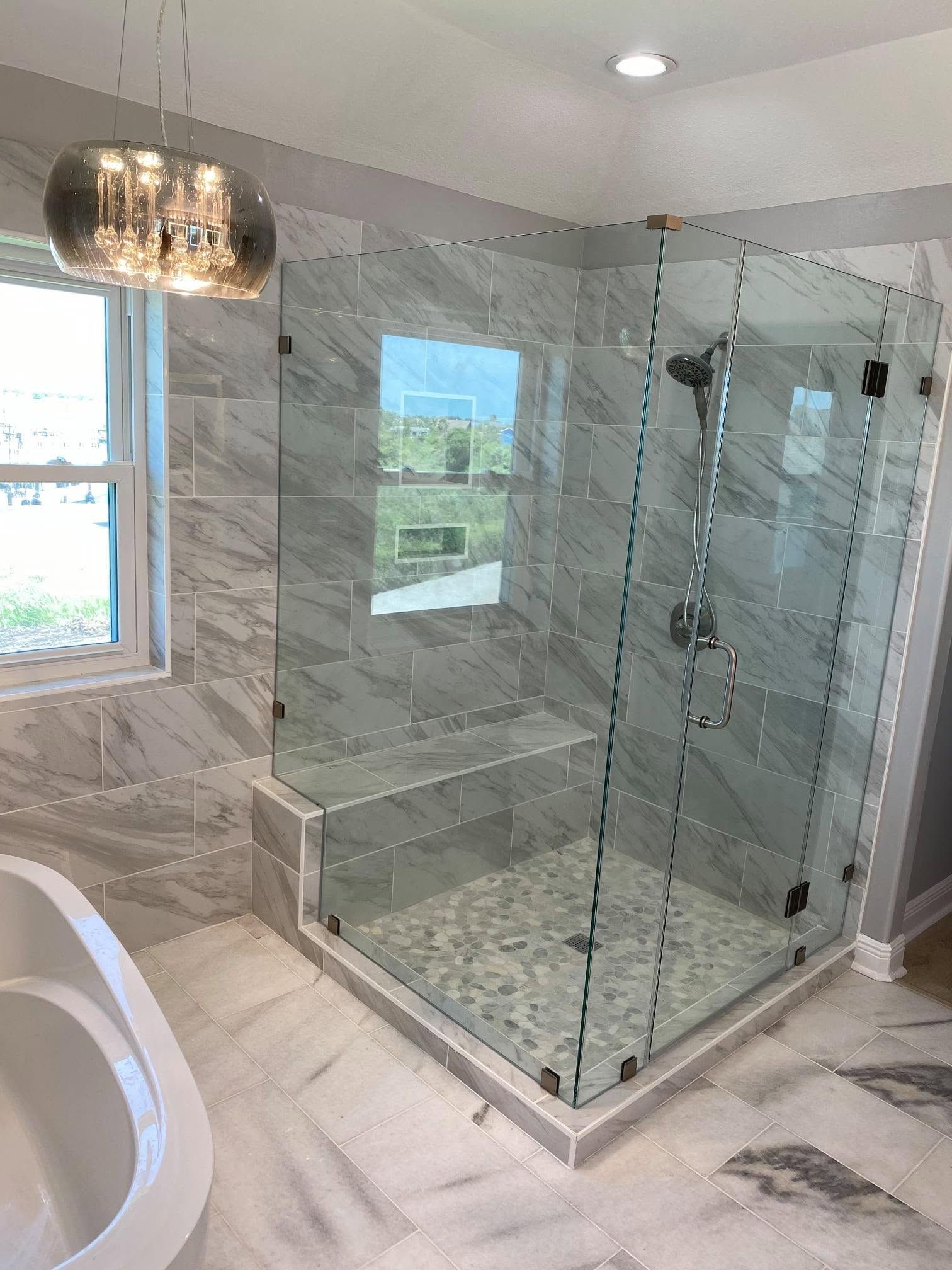 Modern bathroom with marble tile, glass shower enclosure, and chandelier lighting