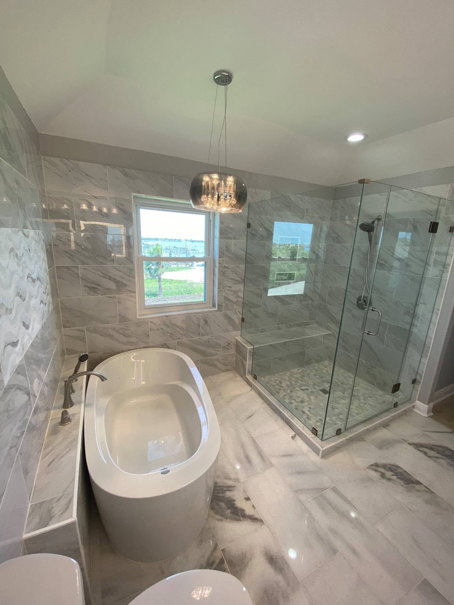 Modern bathroom with a freestanding tub, glass shower, marble tile, and two windows