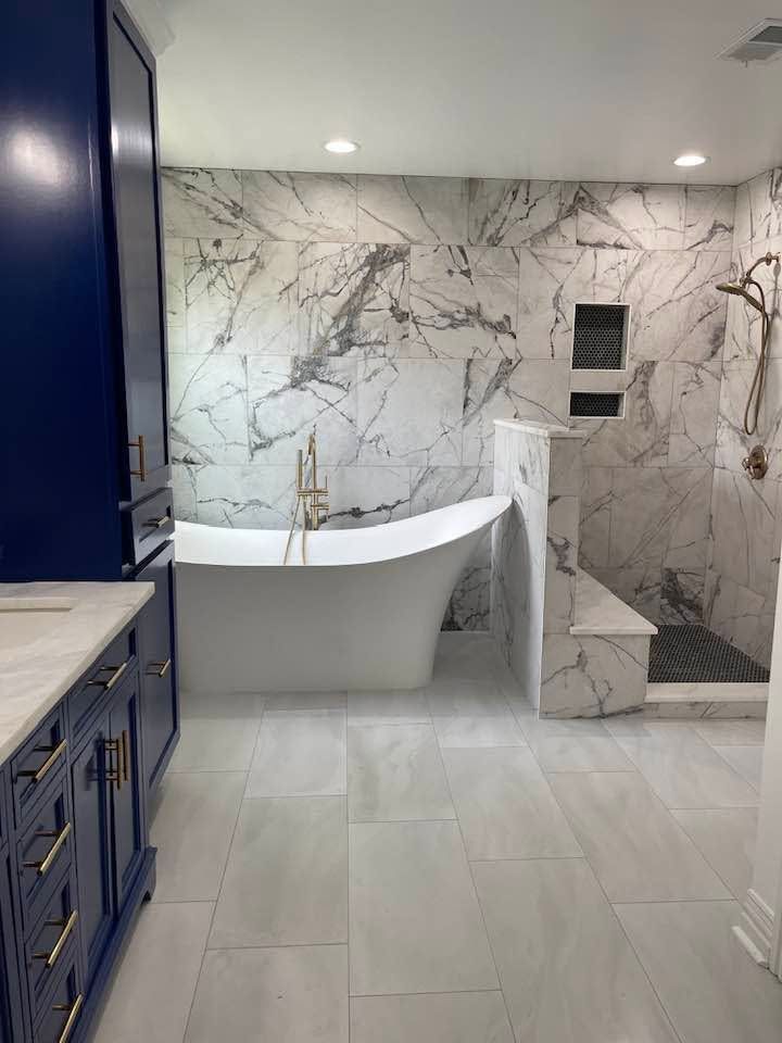 Modern bathroom with marble shower walls, white tub, and navy vanity cabinets