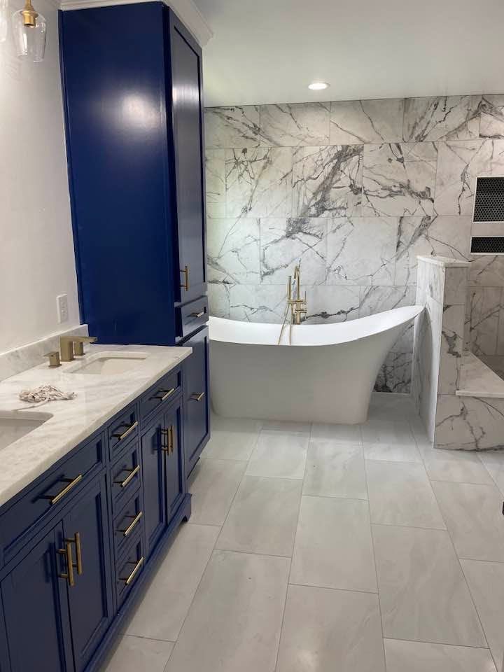Elegant bathroom with navy vanity, marble walls, and a freestanding tub