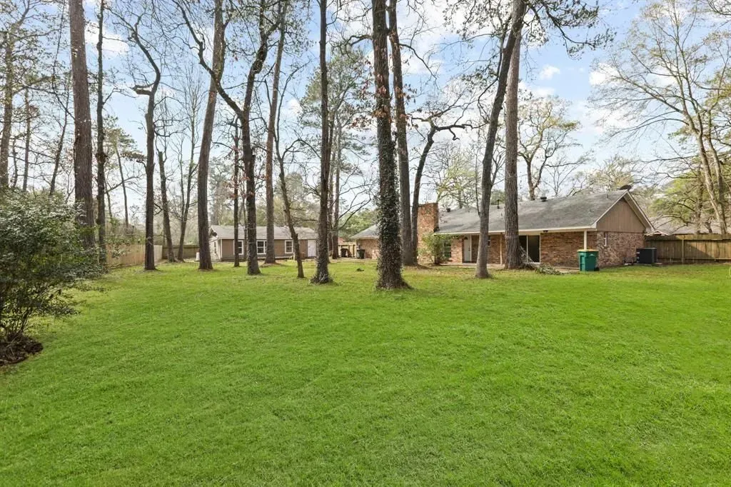 Grassy yard with tall trees and a small house in the background under a cloudy sky