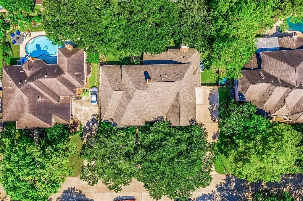 Aerial view of tropical thatched-roof houses surrounded by dense green trees, with a blue pool on the left.
