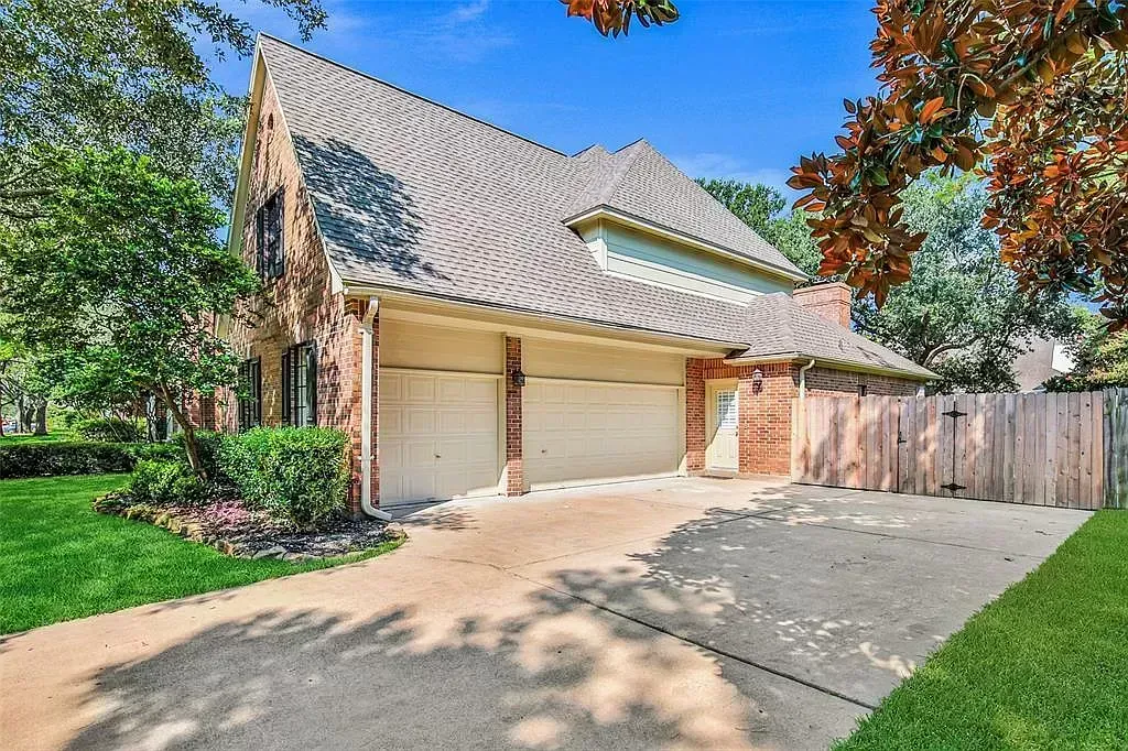 Suburban house with a tiled roof, two-car garage, driveway, and green trees and lawn.