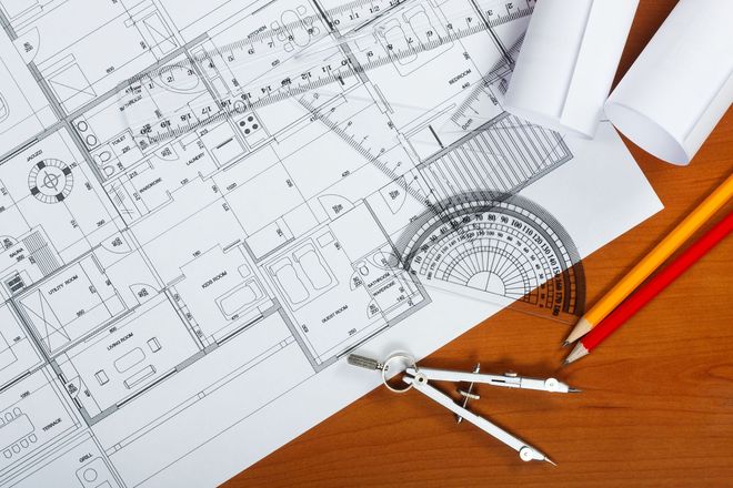 Architectural blueprint with drafting tools, ruler, compass, and red pencil on a wooden desk