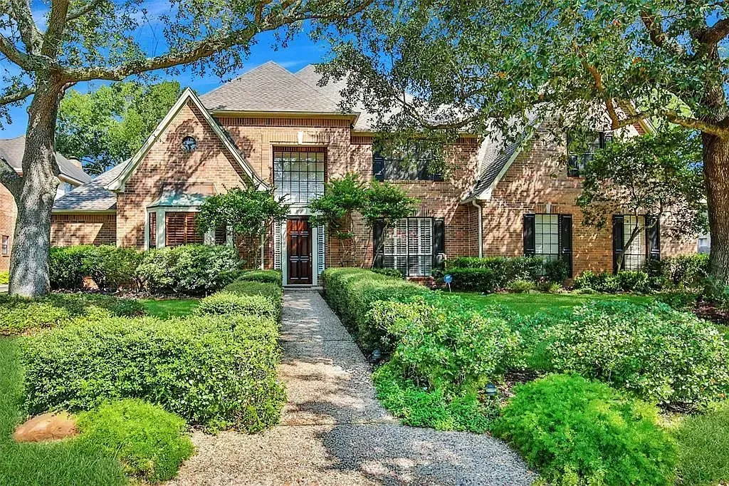 Brick house with a red door, arched windows, and a stone path amid lush green landscaping.