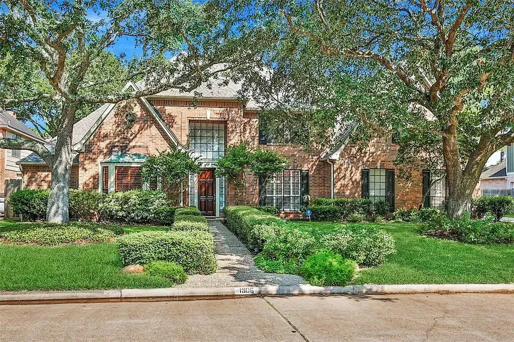Brick house with front garden, large trees, and a walkway along the street