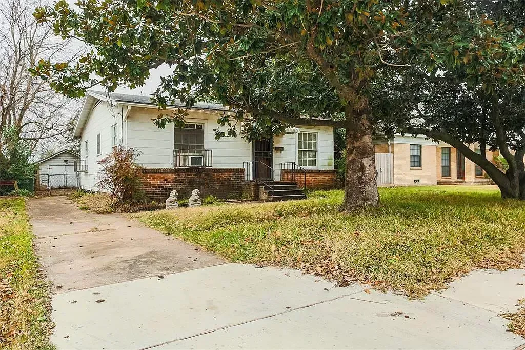 Suburban house with large front yard, driveway, and a tree-covered lawn in autumn.