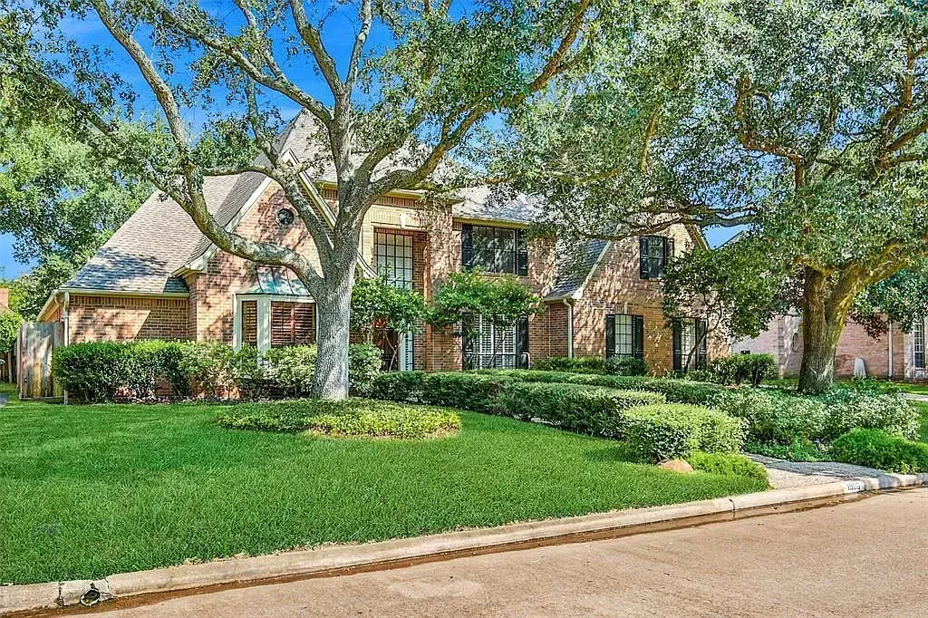Suburban brick house with a green lawn and large trees along the street