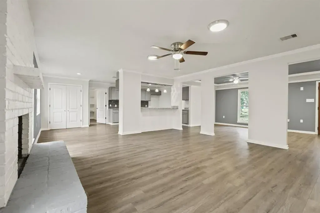 Spacious empty living room with white walls, wood floors, ceiling fan, and large open doorway.