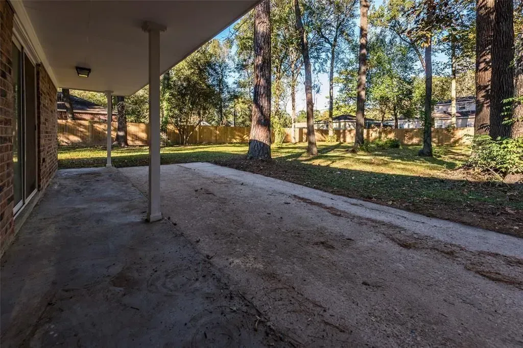 Covered driveway beside a brick house, with trees and lawn in the background.