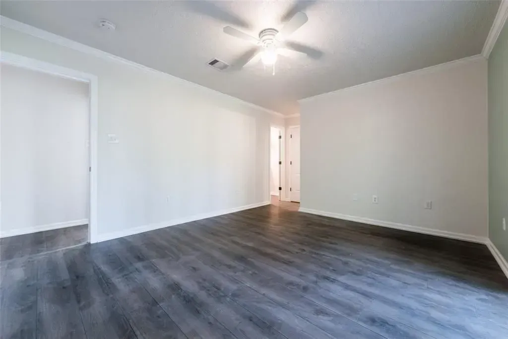 Empty room with gray wood floors, white walls, ceiling fan, and bright doorway.
