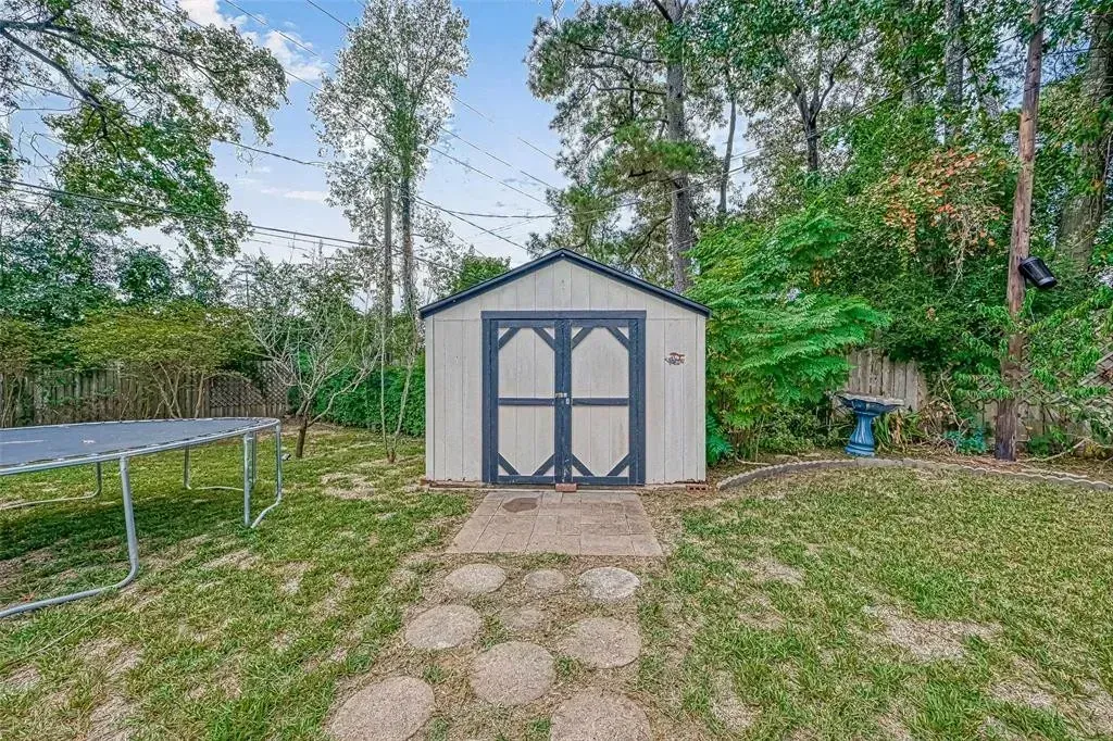 Small gray shed with blue double doors at the end of a gravel path in a wooded yard
