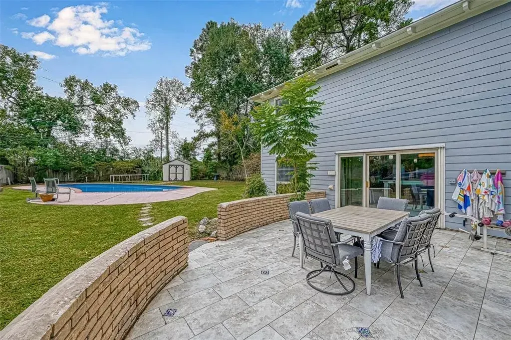 Patio with table and chairs beside a house, overlooking a backyard pool and lawn.