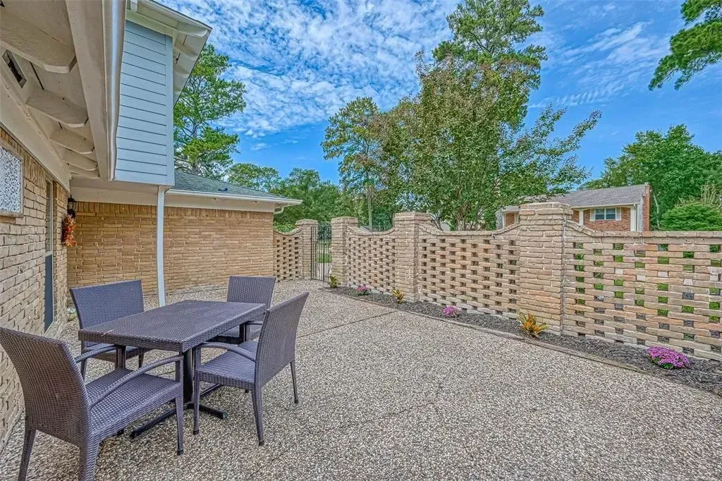 Patio with black table and chairs, gravel ground, brick walls, and trees under a blue sky