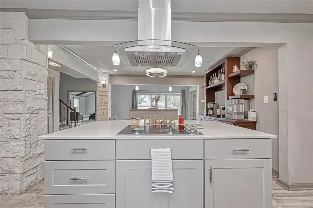 Modern kitchen with large island, white cabinets, stainless range hood, and open shelving