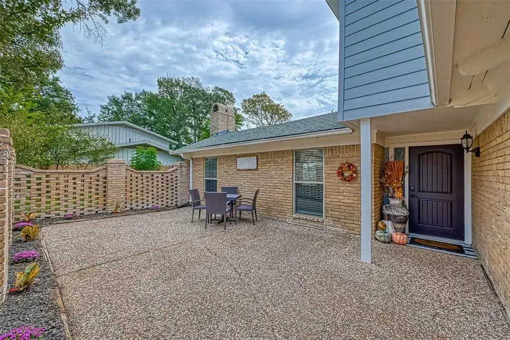 Gravel courtyard beside a house with patio chairs, fence, and a dark front door under a cloudy sky