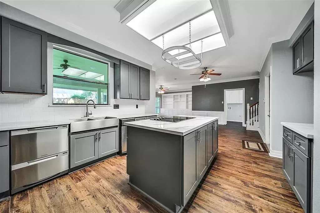 Modern kitchen with gray cabinets, large island, wood floors, and skylight-lit ceiling