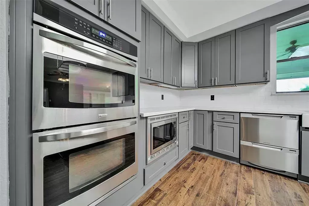 Modern kitchen with stainless steel double ovens, gray cabinets, white counters, and wood flooring