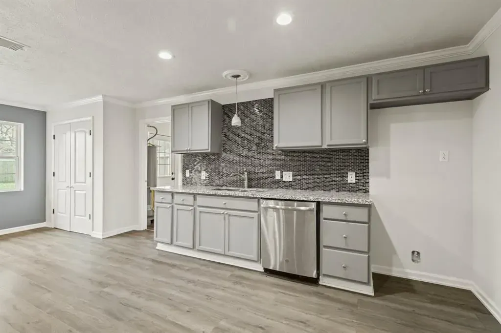 Open kitchen with gray cabinets, stainless appliances, mosaic backsplash, and light wood floors