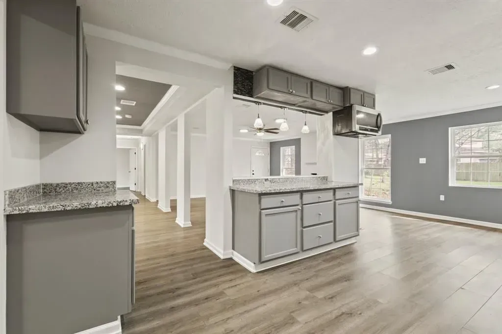 Spacious modern kitchen with gray cabinets, white walls, wood floors, and an island under exposed ductwork