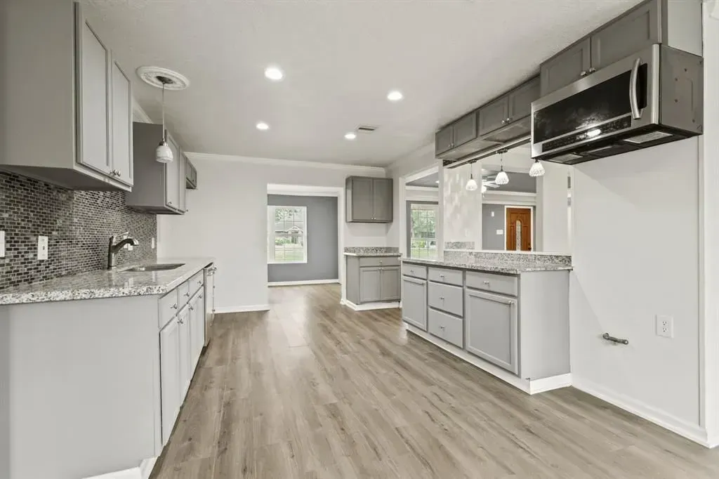 Bright modern kitchen with white cabinets, gray countertops, stainless appliances, and wood-look floors