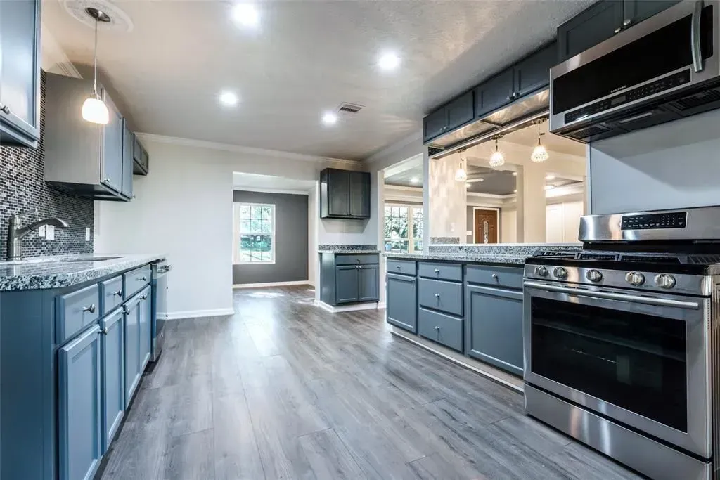 Modern kitchen with blue-gray cabinets, stainless appliances, and wood-look flooring