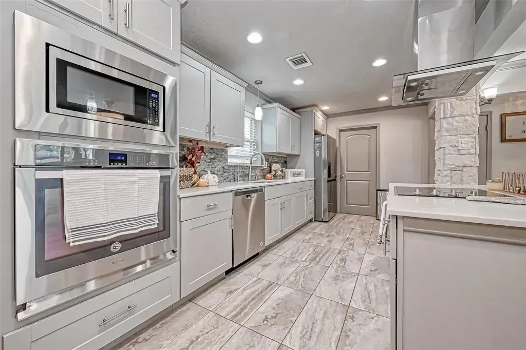 Bright modern kitchen with white cabinets, stainless appliances, and marble-patterned floor, viewed down the aisle