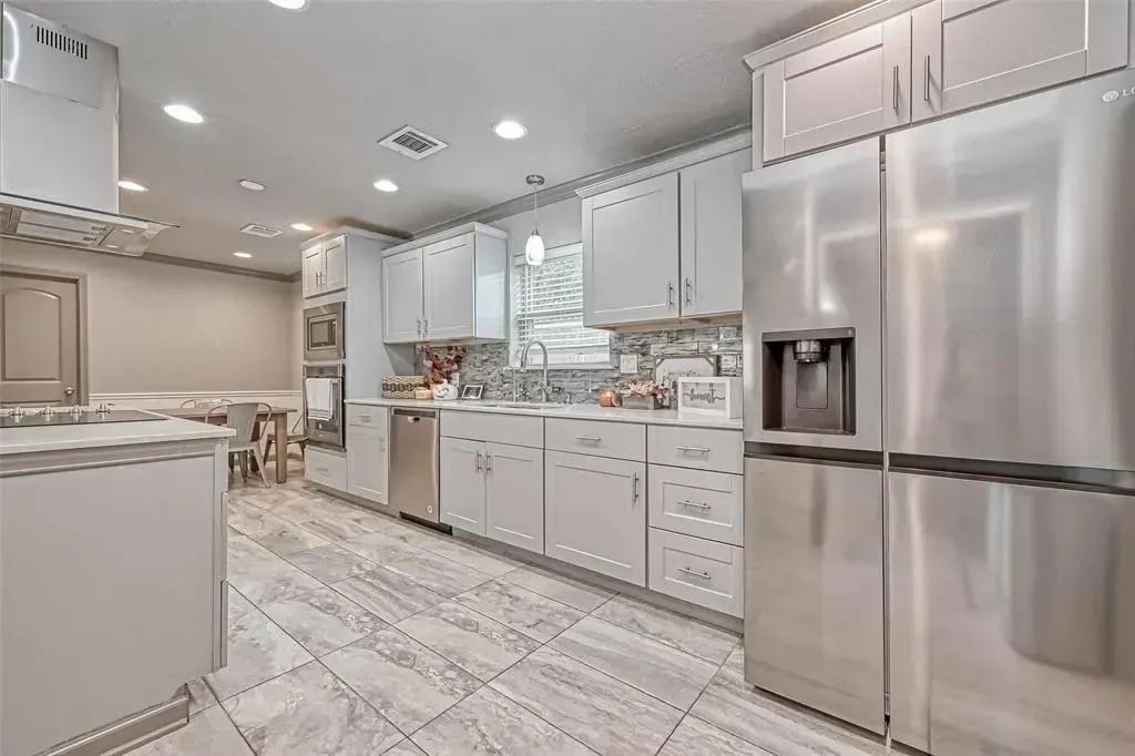 Bright white kitchen with stainless steel refrigerator, marble floor, and island countertop