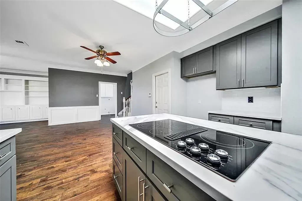 Modern kitchen with gray cabinets, white countertops, and wood floors, viewed from the island toward an open room