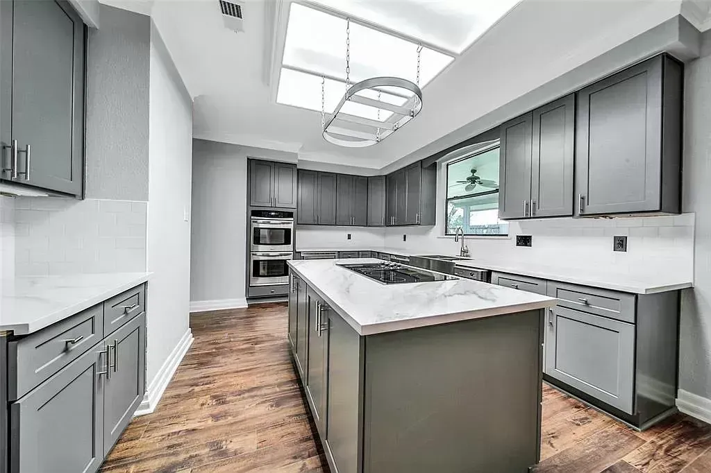 Bright modern kitchen with gray cabinets, white island, and wood flooring under a skylight.